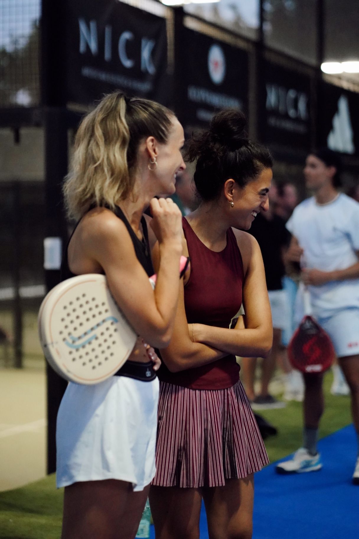 Twee padelspeelsters lachen samen naast de baan
