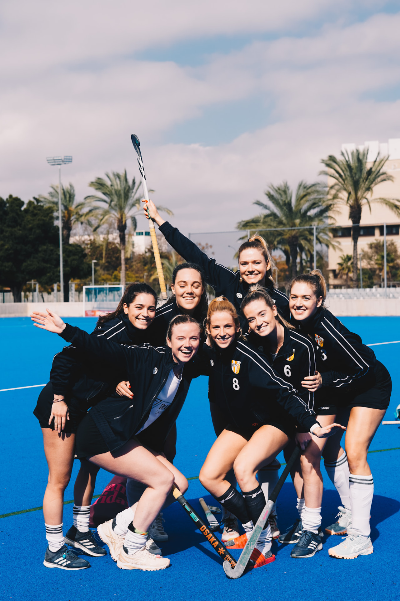 Damesteam poseert lachend op het blauwe hockeyveld met palmbomen