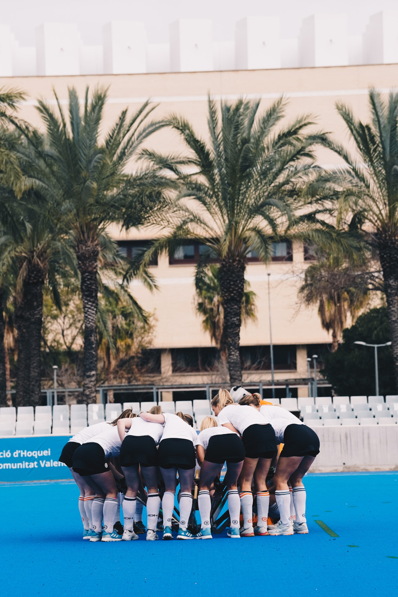 Hockeyteam in huddle op het blauwe veld tussen de palmbomen