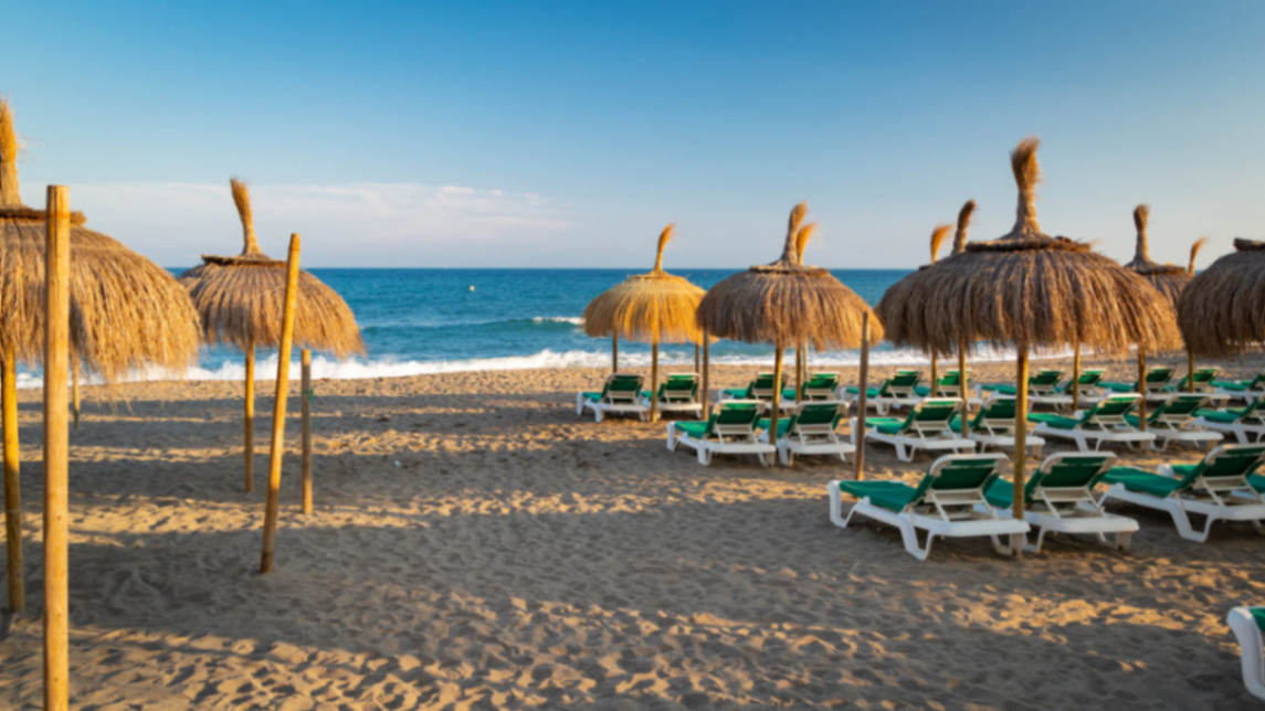 Strandbedjes met rieten parasols aan de Marbella kustlijn