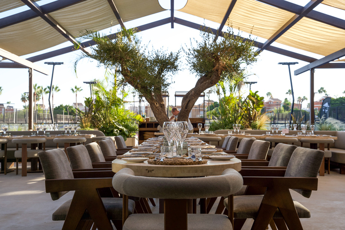 Buitenrestaurant met olijfboom en padelbanen op de achtergrond